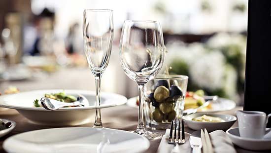 Two polished wine glasses sitting next to tableware on a restaurant table.